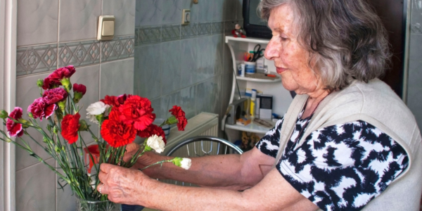 Assess tenants' needs. Older woman arranging flowers in her home.