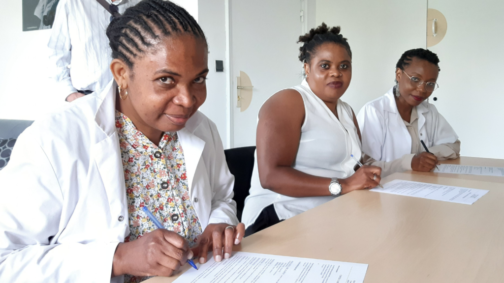 Three women are smiling at the camera while signing contracts. Part of initiative to promote women's economic participation.