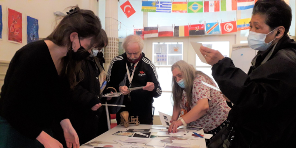 Inside Biloba Huis. A group of people are working around a table with cards with images. At the back, there are different flags.