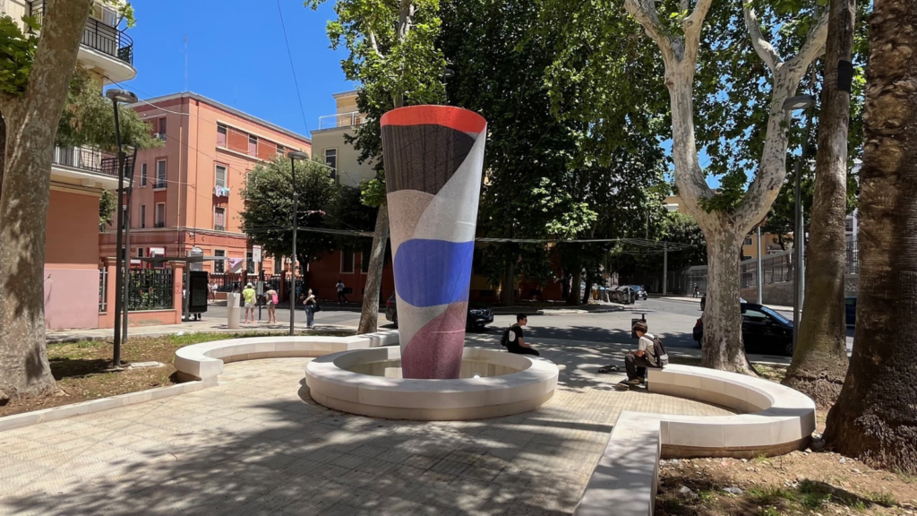 Urban regeneration involving public art. We see a circular fountain space with a modern and colourful artwork on the side of the fountain