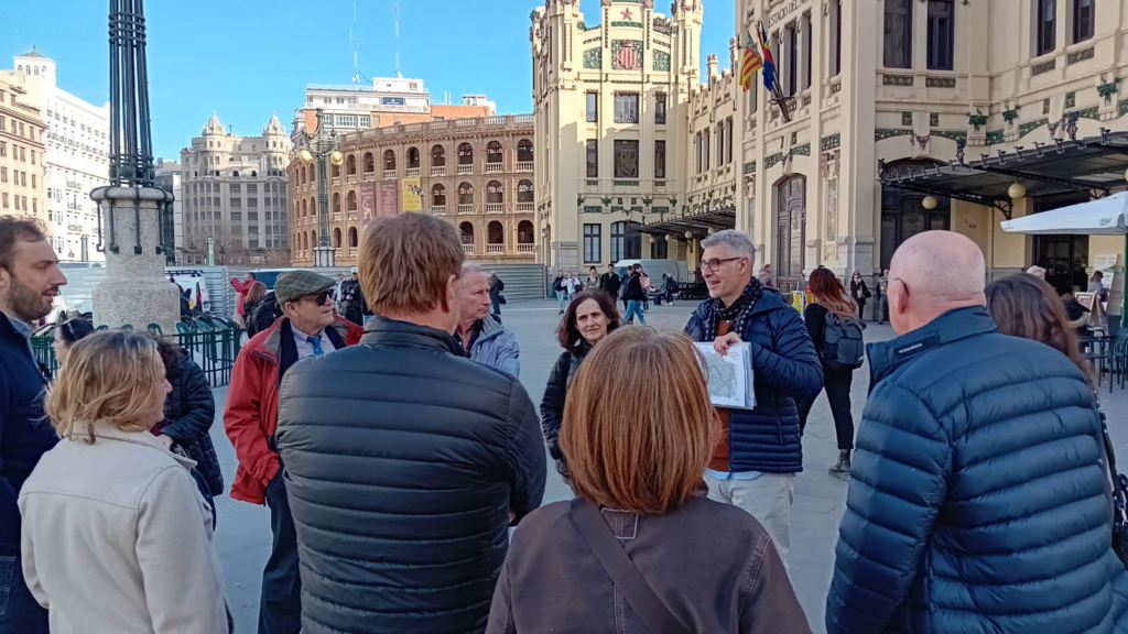 Tour stops outside of Valencia train station. Group photo with guide in the middle showing plans on a paper.